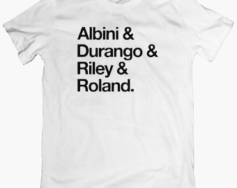 May include: White t-shirt with black text that reads "Albini & Durango & Riley & Roland."