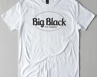 May include: White t-shirt with the words "Big Black" in a black, oval-shaped design. Below the text, the phrase "It's Toasted" is printed in smaller black letters. The shirt has a crew neck and short sleeves.