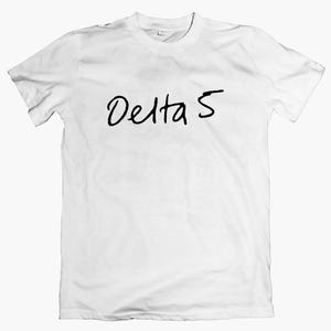 May include: White t-shirt featuring the black handwritten text "Delta 5". The top has a crew neck and short sleeves. The material looks soft and lightweight.