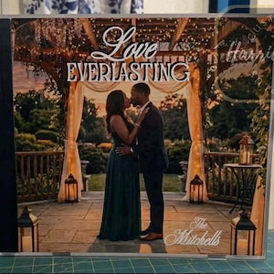 May include: A custom photo print showing a couple kissing under a gazebo with the words "Love Everlasting." The couple is in formal attire. The print includes the names "Harriett's Computer Art" and "The Mitchells."