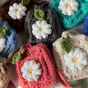 May include: A collection of 11 crocheted flower-shaped pouches in various colors, including pink, blue, green, brown, and red. Each pouch features a white crocheted flower with a yellow center.