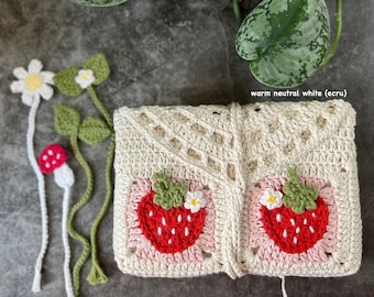 May include: A crocheted pouch with a warm neutral white (ecru) color. The pouch features two strawberry designs with green leaves and white flowers. The pouch is closed with a white crocheted tie.
