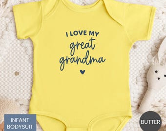 Puede incluir: Un body de bebé amarillo con el texto "I LOVE MY great grandma" en escritura azul marino. Un corazón azul marino está debajo del texto. Las palabras "INFANT BODYSUIT" están en un rectángulo azul.