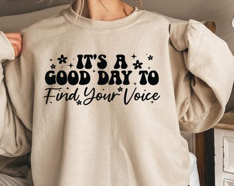 Può includere: Felpa beige con la scritta nera "IT'S A GOOD DAY TO Find Your Voice", decorata con piccoli fiori e stelle. La felpa ha un girocollo e maniche lunghe.
