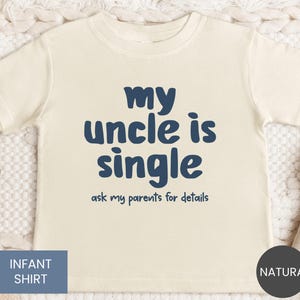 May include: Cream-colored infant shirt with navy blue text that reads "my uncle is single ask my parents for details". The shirt has short sleeves and a crew neck. The words "Infant Shirt" are in a blue box.
