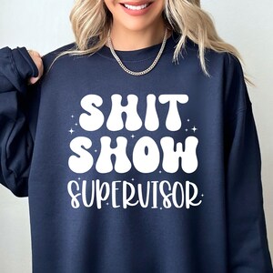 a woman wearing a sweatshirt that says shit show supervisor