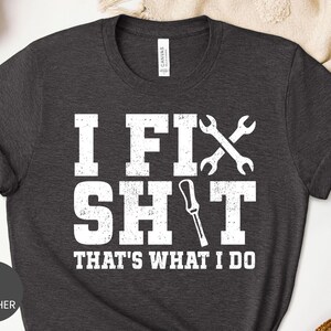 May include: A dark grey heather short-sleeve t-shirt with white distressed text that reads I FIX SH*T THAT'S WHAT I DO. The design includes a graphic of two crossed wrenches and a screwdriver replacing the letter I in the word SH*T.