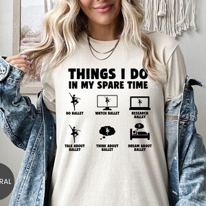 May include: A beige t-shirt with the text "THINGS I DO IN MY SPARE TIME" and ballet-themed icons. The shirt lists activities like "DO BALLET," "WATCH BALLET," and "DREAM ABOUT BALLET." The word "NATURAL" is printed on a circle at the bottom.