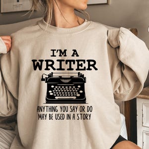 May include: A beige sweatshirt with the text "I'm a writer" and a vintage typewriter graphic. The text below the graphic reads "Anything you say or do may be used in a story."