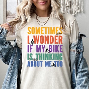 May include: A cream colored t-shirt with the text "Sometimes I wonder if my bike is thinking about me too" in rainbow colors with a small bicycle graphic next to each word.