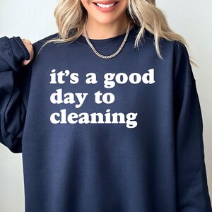 May include: Navy blue sweatshirt with the phrase "it's a good day to cleaning" in white block letters. The crew neck sweatshirt is a casual style.