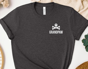 Op de afbeelding: Donkergrijs T-shirt met een witte afbeelding van gekruiste botten met een pootprint erboven en de tekst "GRANDPAW" eronder.