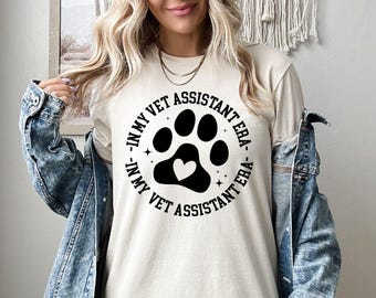 May include: A white t-shirt with a black paw print design and the text "In My Vet Assistant Era - In My Vet Assistant Era".