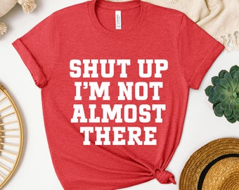 May include: Red t-shirt with white text that reads "Shut Up I'm Not Almost There".
