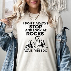 May include: A white t-shirt with black text that reads "I don't always stop and look at rocks. Wait, yes I do."  The text is surrounded by a graphic of three rock formations.