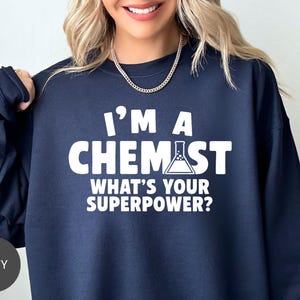 May include: Navy blue sweatshirt with the text "I'M A CHEMIST WHAT'S YOUR SUPERPOWER?" in white block letters. A beaker graphic is included in the word "CHEMIST". The sweatshirt is a crew neck style.