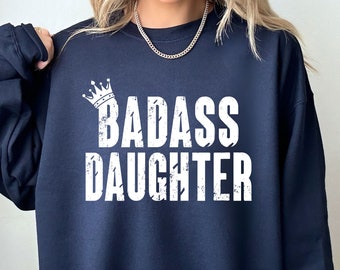 May include: A navy blue sweatshirt with a white crown and the text "BADASS DAUGHTER" in a distressed font.