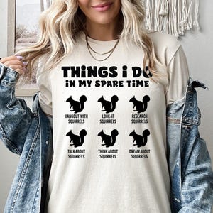 May include: A white t-shirt with black text that reads "Things I Do In My Spare Time" and features six black silhouettes of squirrels with text below each squirrel that reads "Hangout with Squirrels", "Look at Squirrels", "Research Squirrels", "Talk About Squirrels", "Think About Squirrels", and "Dream About Squirrels".