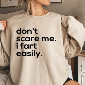 May include: A beige sweatshirt with the text "don't scare me. i fart easily." printed in black.