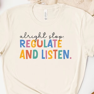 May include: A white t-shirt with the text "alright stop. REGULATE AND LISTEN." in colorful letters.