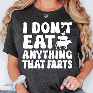 May include: A dark gray t-shirt with the text "I don't eat anything that farts" in white. The text is in a retro font style. There is a white silhouette of a chicken, pig, and cow stacked on top of each other.