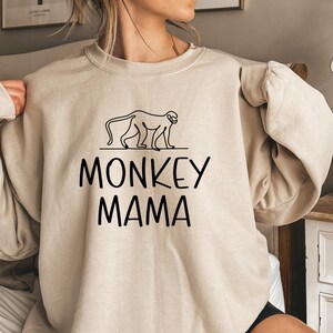May include: A beige sweatshirt with a black outline of a monkey and the text "MONKEY MAMA" printed on the front.