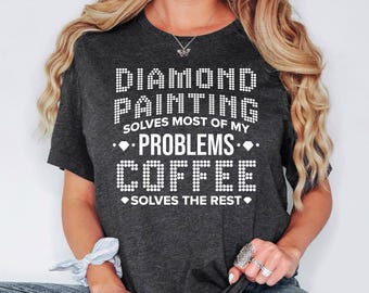 May include: Dark gray t-shirt with white text that reads "DIAMOND PAINTING solves most of my PROBLEMS COFFEE solves the rest." The text is in a dotted font. The shirt is a crew neck.