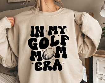 May include: A beige sweatshirt with the text "In My Golf Mom Era" in black with a golf ball graphic.