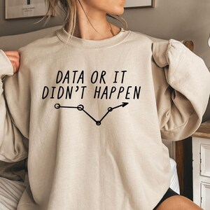 May include: A beige sweatshirt with the text "DATA OR IT DIDN'T HAPPEN" in black, along with a black line graph design. The sweatshirt has a crew neck and long sleeves.