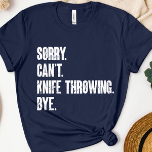 May include: A navy blue t-shirt with white text that reads "Sorry. Can't. Knife Throwing. Bye."