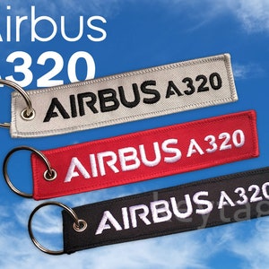 May include: Three keychains with the text "AIRBUS A320" on them. The keychains are in three different colors: gray, red, and black. The keychains are against a blue sky background with white clouds.