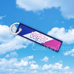 May include: Blue and pink luggage tag with a white stripe and the word "Wizz" in white letters. The tag has a silver key ring.