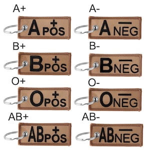 May include: Eight brown fabric keychains with metal rings. Each keychain has a white embroidered letter and the words "POS" or "NEG" in white. The letters represent blood types: A+, A-, B+, B-, O+, O-, AB+, AB-.