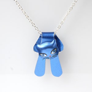 May include: A silver chain necklace with a blue cat pendant. The cat is facing forward with its eyes open and its mouth closed. The cat's ears are pointed and its tail is curled up.