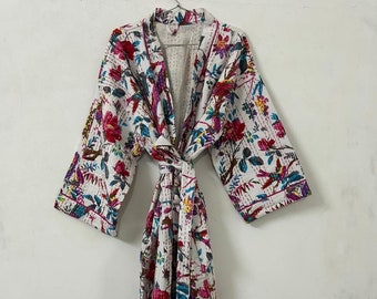 May include: A white cotton robe with a floral print in shades of pink, blue, and green. The robe has a long, flowing silhouette and a tie belt.