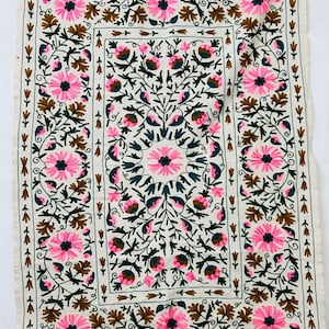Peut inclure: Un tissu en coton blanc avec un motif de broderie florale. La broderie présente des fleurs roses, brunes et vertes avec un motif central d'une fleur plus grande.