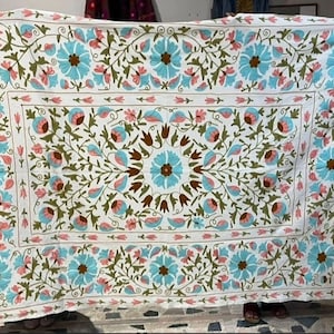 Pode incluir: Cobertor de algodão branco com um design de bordado floral. O bordado apresenta flores azuis, cor-de-rosa e verdes sobre um fundo branco.