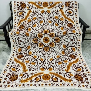 May include: White cotton throw blanket with intricate embroidery in brown and gold floral patterns. The design features a central medallion with repeating motifs throughout.