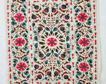 May include: Cream textile with detailed floral embroidery. The design showcases large red flowers with blue centres, surrounded by blue leaves and brown stems. The border is decorated with red tulip-like shapes.