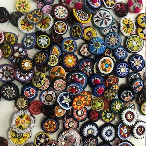 Op de afbeelding: Assortiment van kleurrijke ronde kralenversieringen met kleine spiegels in het midden. Elk ornament is uniek met verschillende patronen en kleuren kralen.