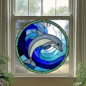 May include: Stained glass window panel featuring a dolphin leaping through blue and turquoise waves. The dolphin is light gray with a white belly, set within a circular frame with a green border. The window is set in a white frame.