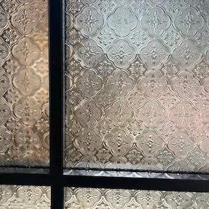 Puede incluir: Primer plano de una ventana con marco negro y cristales transparentes. El vidrio tiene un patrón decorativo de formas de trébol de cuatro hojas que se repiten.