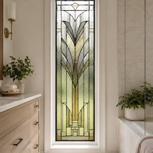 Peut inclure: Une fenêtre haute et rectangulaire en vitrail présentant un motif géométrique symétrique avec des lignes verticales et un motif végétal stylisé central dans des tons de vert pâle, ambre et verre texturé clair, encadrée en blanc.