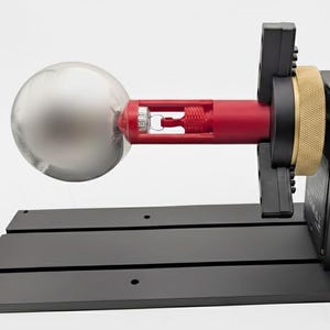 Könnte beinhalten: Eine schwarz-rote Maschine mit einer silbernen Kugel, montiert auf einer schwarzen Basis. Die Maschine hat eine rote zylindrische Komponente, ein goldfarbenes Band und ein schwarzes Bedienfeld mit einem Knopf "FASTER".