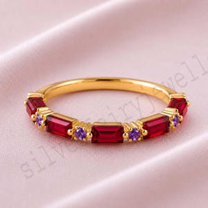 May include: A gold band ring featuring an alternating pattern of rectangular baguette-cut red stones and small round purple stones set along the front half of the band. The metal has a polished yellow gold finish and a smooth, rounded inner surface.