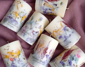 Peut inclure: Un ensemble de sept bougies cylindriques avec des fleurs séchées et des plantes botaniques incorporées dans la cire. Les bougies sont blanches avec une teinte jaune clair et portent une étiquette indiquant "Botanical Candle 100% natural wax" et "by Candle Fee Rapswachs".