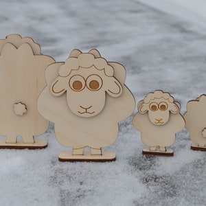 Puede incluir: Cuatro figuritas de ovejas de madera, dos con caras y dos sin, de pie sobre una superficie nevada.