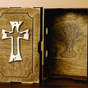 Może przedstawiać: Drewniane pudełko na Biblię z otwartą pokrywą. Przód pudełka zdobi biały krzyż i napis „HOLY BIBLE”. Wnętrze pudełka ma wzór drzewa.