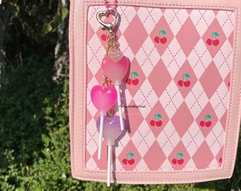 May include: A pink and white checkered handbag with a silver chain and heart-shaped lollipop charms. The bag has a top handle and a detachable strap.