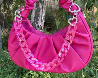 May include: A pink handbag with a chunky iridescent pink chain strap and silver heart-shaped clasps. The bag has a gathered, pleated design.